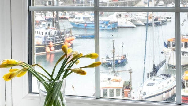 A window with a view of a harbor, a vase with yellow flowers, and a white window frame.