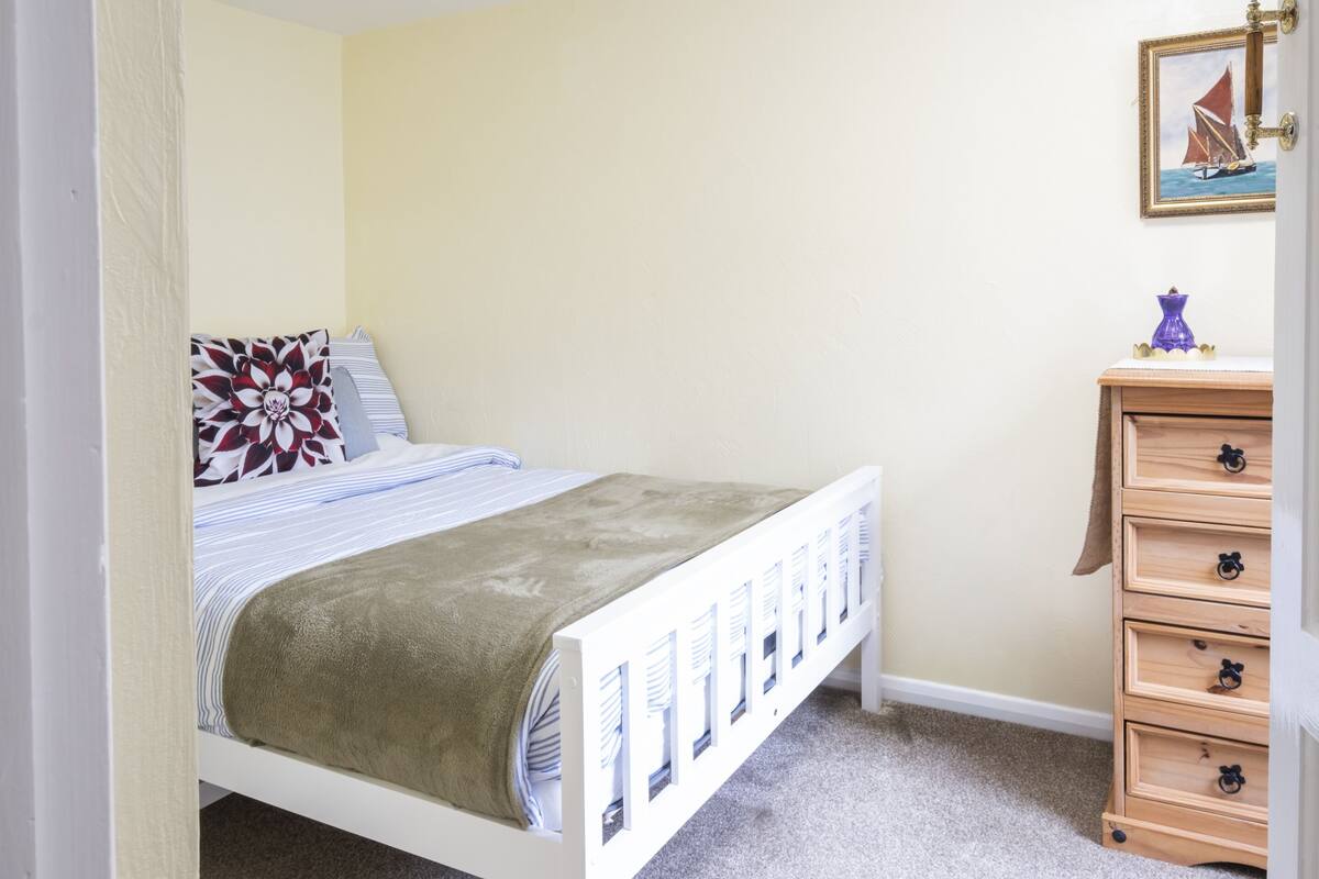 A bedroom with a bed, a dresser, a framed picture, and a carpeted floor.