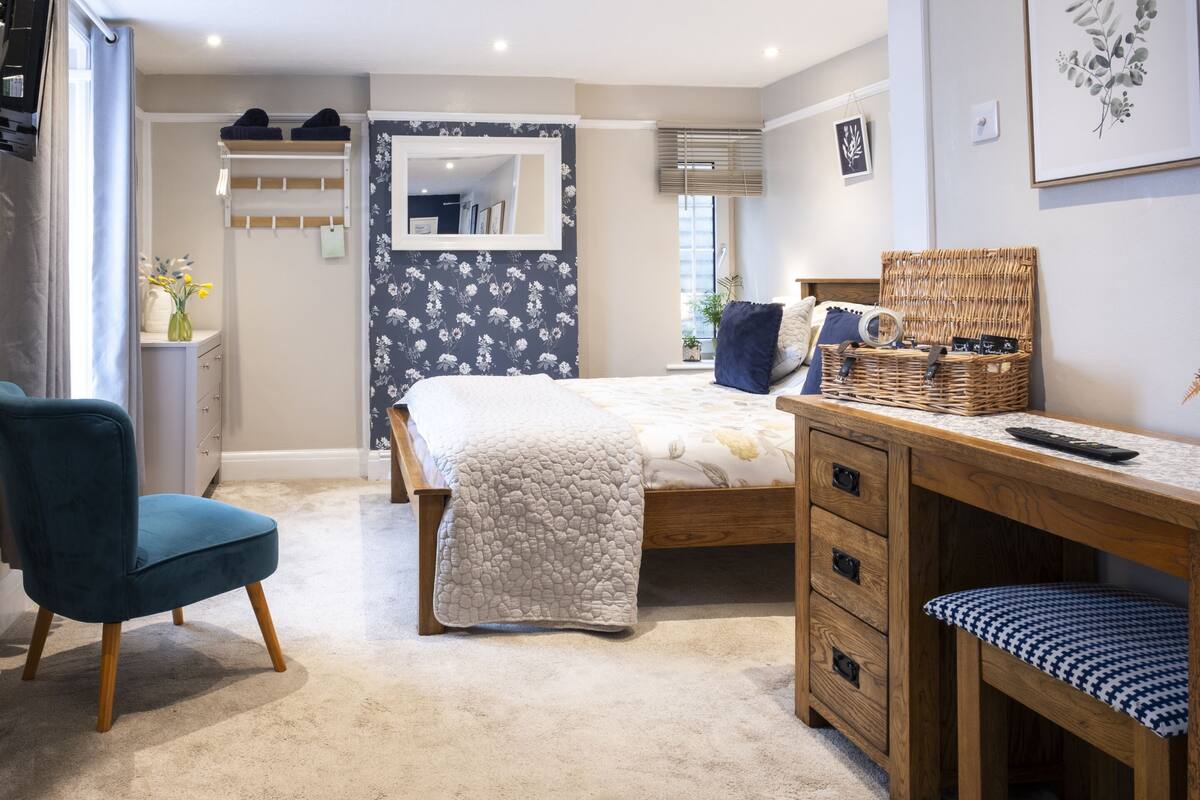 A bedroom with a bed, a desk, a chair, a dresser, a mirror, and a window with blinds.