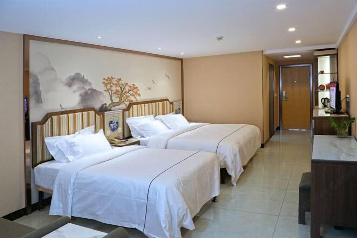 Ein Hotelzimmer mit zwei Betten, einem kleinen Schreibtisch, einem Stuhl und einer Wanddekoration.