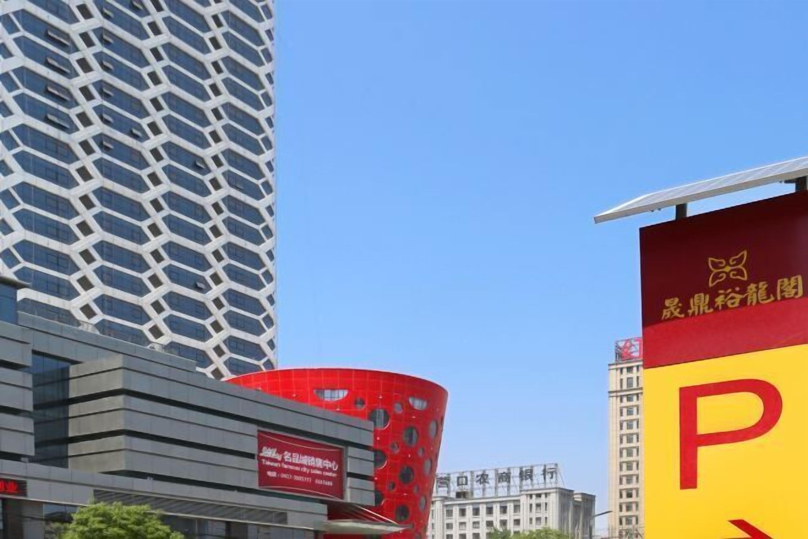 A modern building with a unique geometric facade, a prominent red structure with circular cutouts, and a large yellow sign with a red 'P' indicating parking.