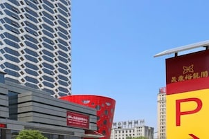Un edificio moderno con una fachada geométrica única, una estructura roja destacada con círculos recortados y un letrero amarillo grande con una 'P' roja que indica estacionamiento.