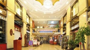 A hotel lobby with a central staircase, a reception desk, and a chandelier.