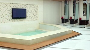 A modern spa area with a large bathtub, a television mounted on the wall, and a tiled mosaic design.