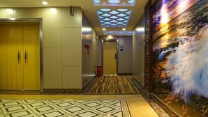 A hotel lobby with a patterned floor, a large wall mural, and a ceiling with a geometric light fixture.