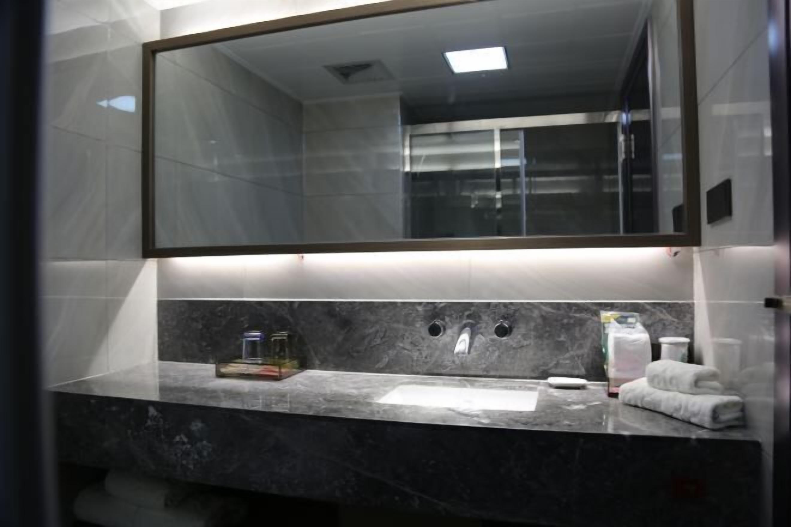 A modern bathroom with a large mirror, a marble countertop, a sink, and a towel rack.