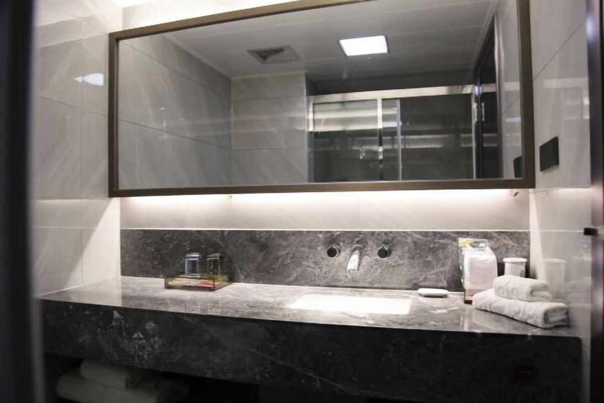 A modern bathroom with a large mirror, marble countertop, and a glass shower enclosure.