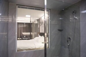 A modern bathroom with a glass shower enclosure, a visible bed with white linens, and a showerhead. - Yingkou Yudingyu Longge Business Hotel 1 (Wanda Plaza) (Yingkou)