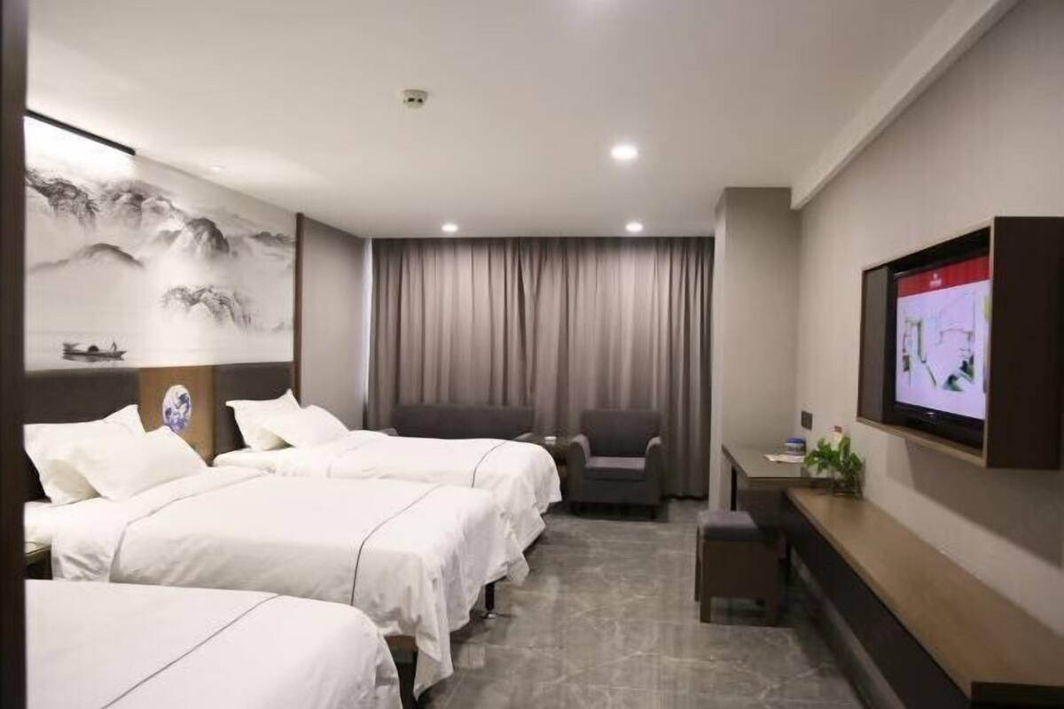 Ein Hotelzimmer mit zwei Betten, einem Schreibtisch, einem Sessel, einem Fernseher und einem Gemälde an der Wand.