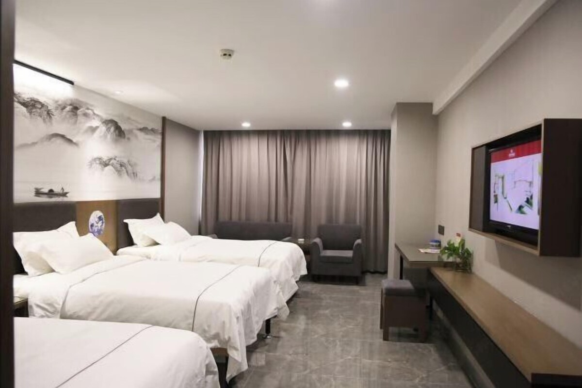 A hotel room with two beds, a desk, a chair, a TV, and a painting on the wall.