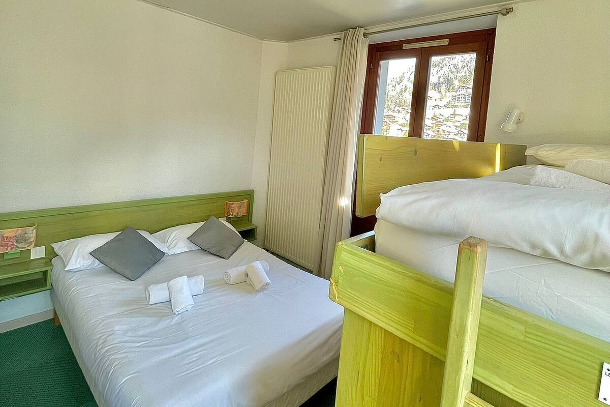 Une chambre avec deux lits, une fenêtre avec des rideaux et une moquette verte.