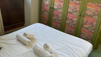 A neatly made bed with white linens and rolled towels, a green upholstered headboard with floral patterns, and a green carpeted floor.