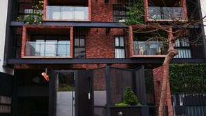 A modern multi-story building with a brick facade, large windows, and a gated entrance. - The Luxus Flat Miraflores (Lima)
