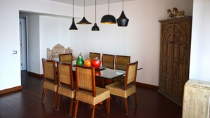 A dining area with a glass table surrounded by wicker chairs, black pendant lights, and a wooden cabinet with decorative items. - The Luxus Flat Miraflores (Lima)