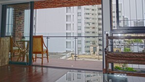 A balcony with a wicker chair and a wooden bench, overlooking a cityscape with high-rise buildings. - The Luxus Flat Miraflores (Lima)