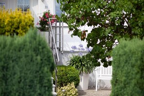 Un bâtiment blanc portant le numéro 25, un escalier en métal et diverses plantes en pot.