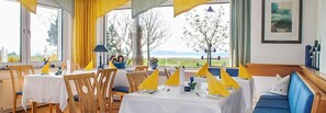 A dining area with tables set for two, chairs, and a view of the outdoors.