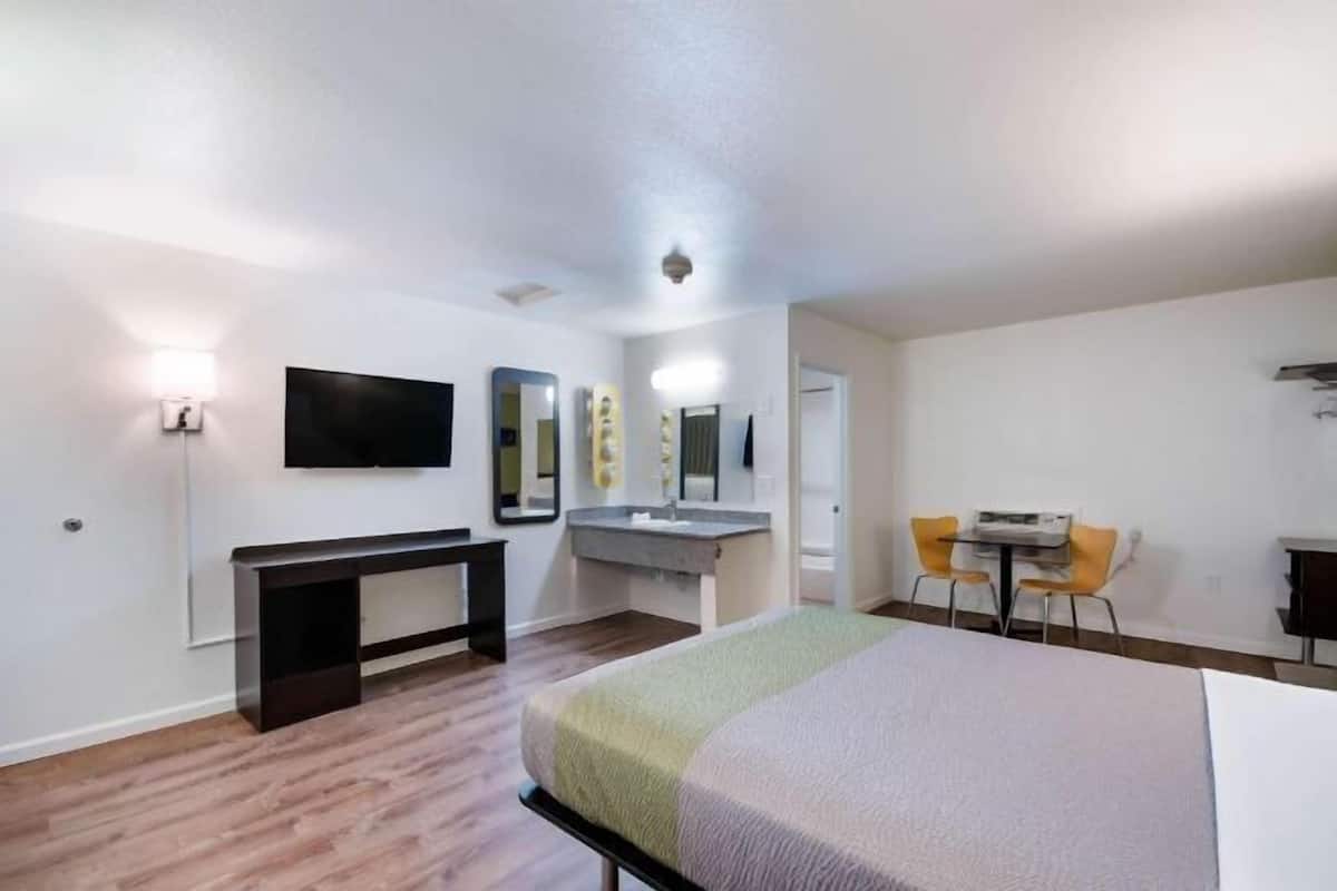 A hotel room with a bed, a desk, a chair, a TV, a mirror, and a bathroom.