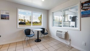 Una habitación con dos sillas alrededor de una mesita, ventanas amplias con vistas al exterior y un aire acondicionado instalado en la pared.