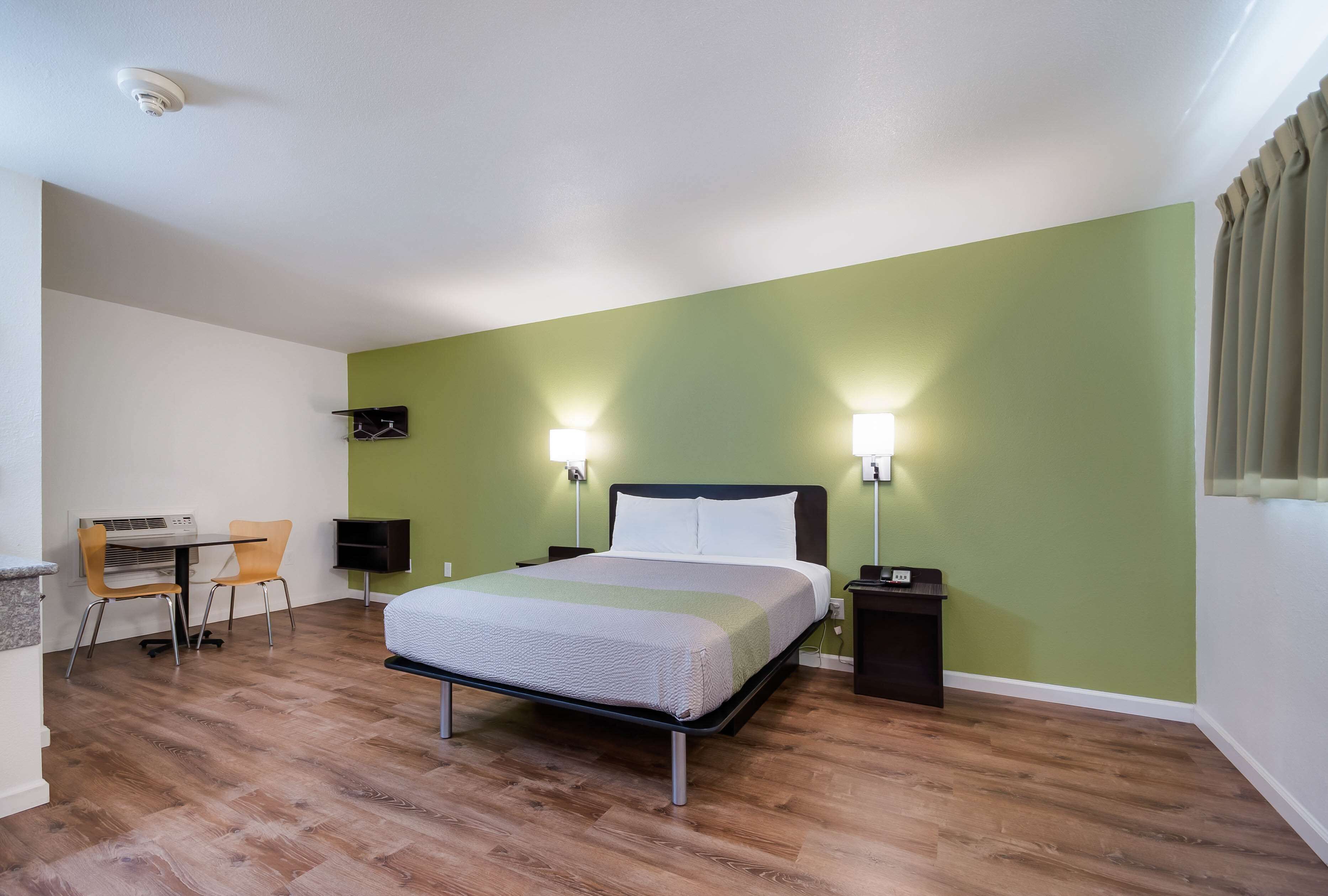 Een hotelkamer met een bed, twee nachtkastjes, een bureau met stoel en een kleine eettafel met stoel.