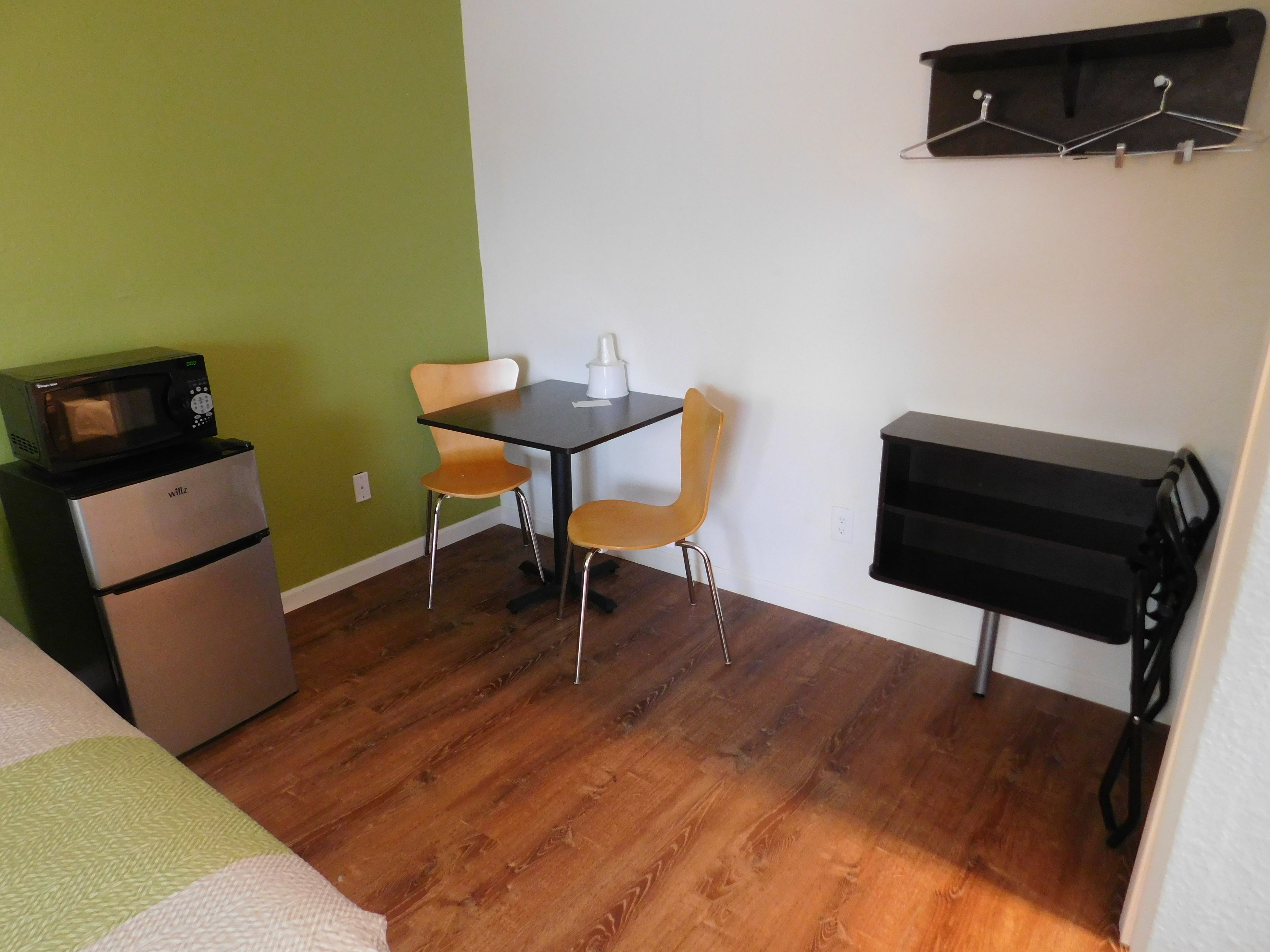 Una habitación compacta con kitchenette, dos sillas, una mesita y un estante negro.