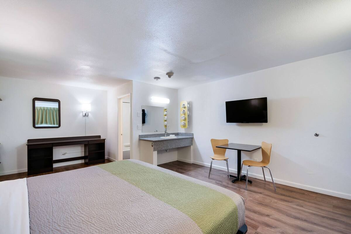 A hotel room with a bed, a desk, a chair, a TV, a mirror, and a bathroom.
