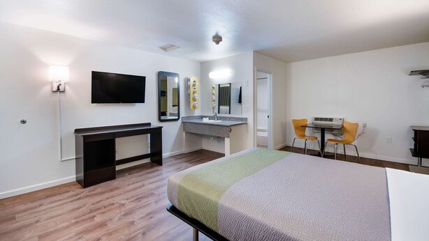 Habitación de hotel con cama, escritorio, silla, televisión, espejo y baño.