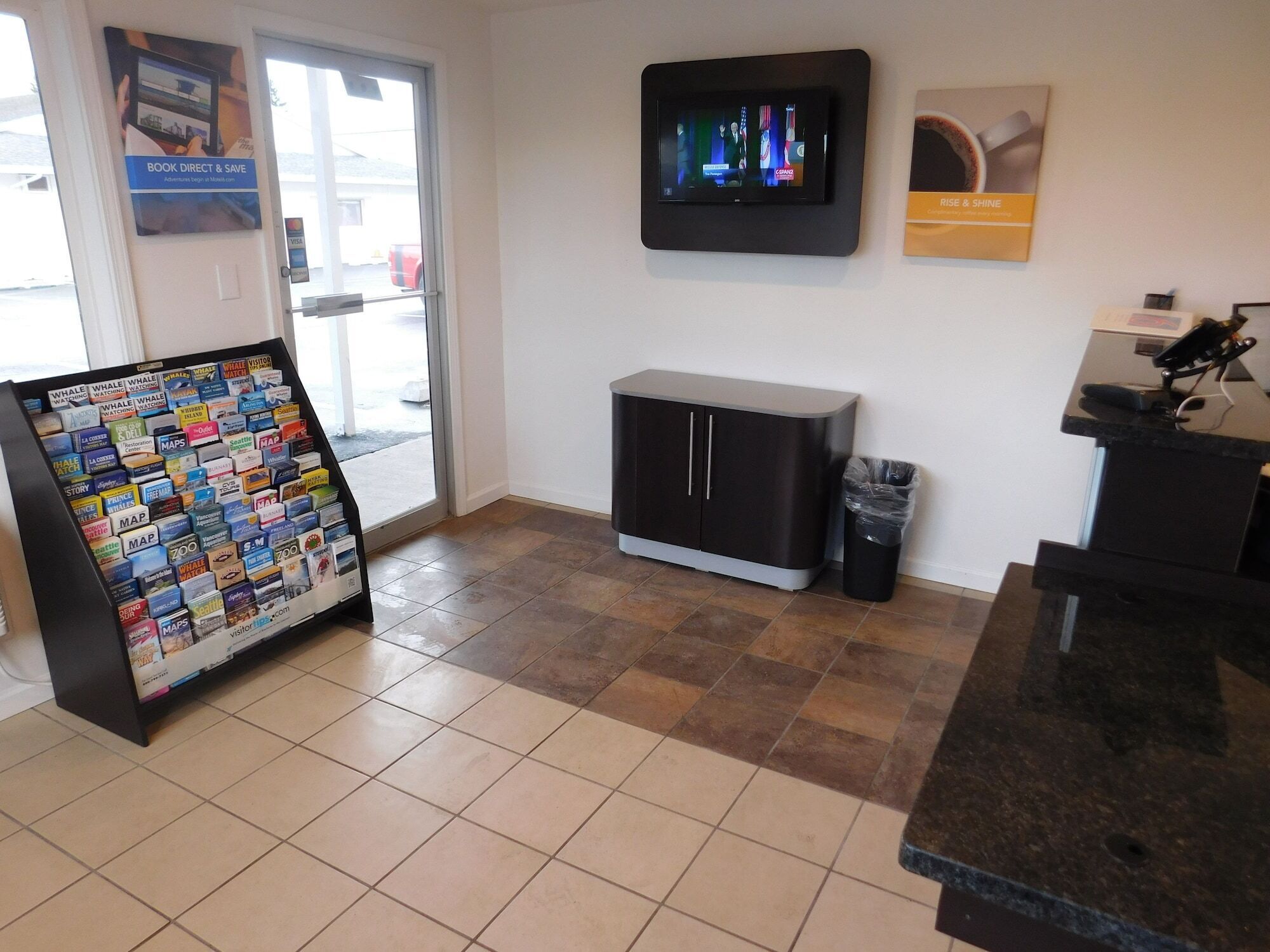 A reception area with a digital screen, a map display, a trash bin, and a small cabinet.