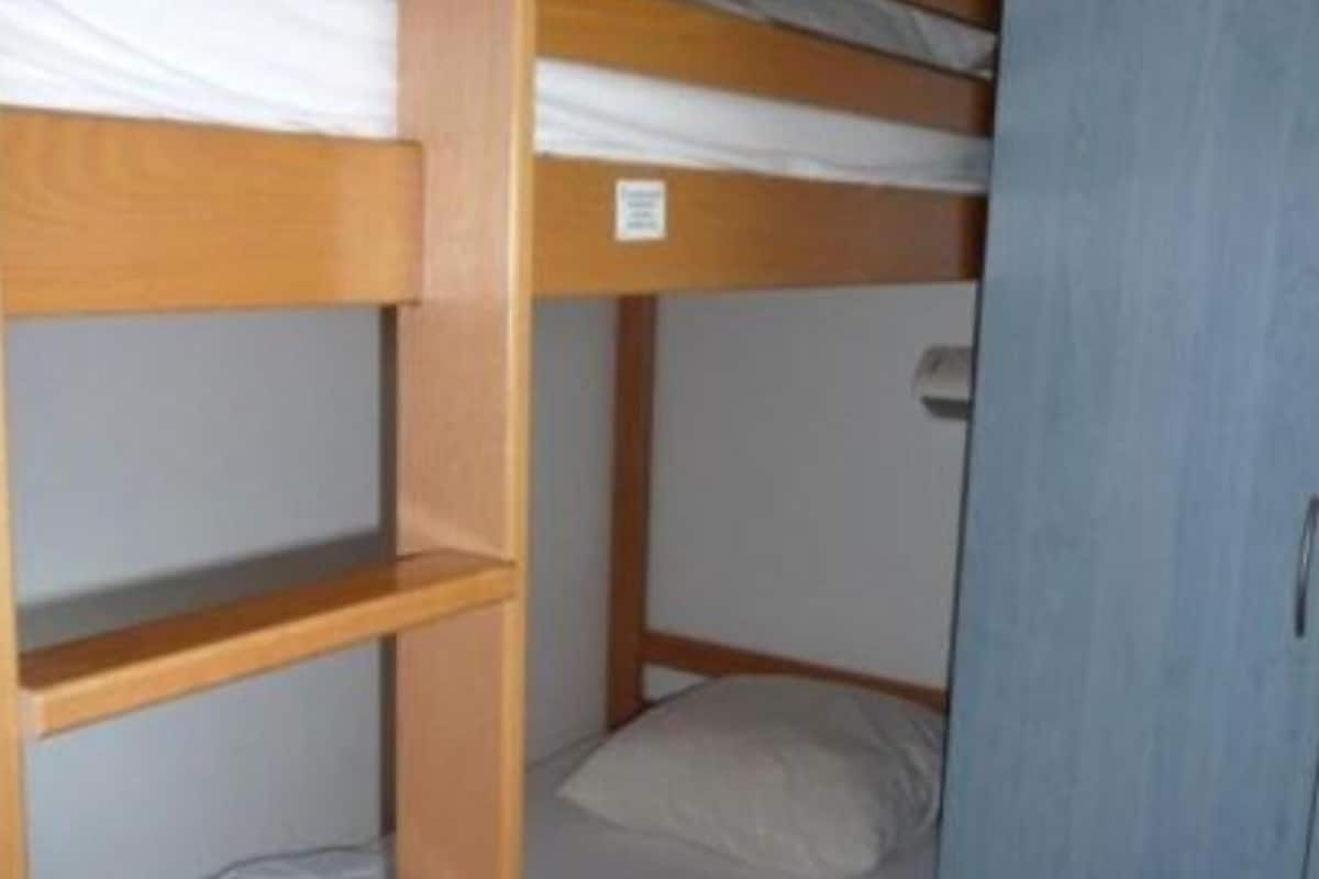 Een stapelbed met een houten trap, een enkel bed en een blauwe garderobe.
