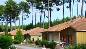 A row of single-story cottages with tiled roofs, surrounded by greenery and trees. - Village Vacances Le Lac Marin Soustons (Soustons)