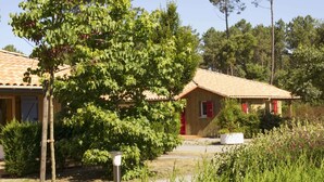 A rustic wooden house with a tiled roof, surrounded by lush greenery and trees. - Village Vacances Le Lac Marin Soustons (Soustons)