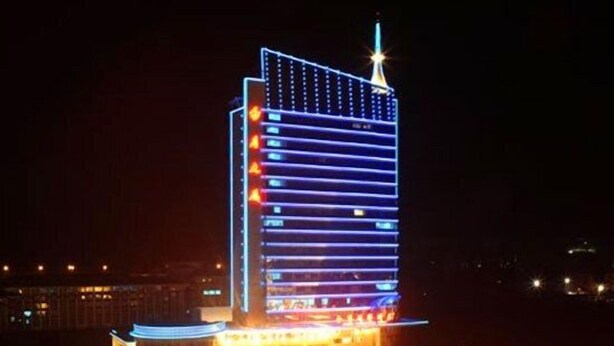 A high-rise hotel with a modern design, featuring a prominent tower with illuminated windows and a spire on top.