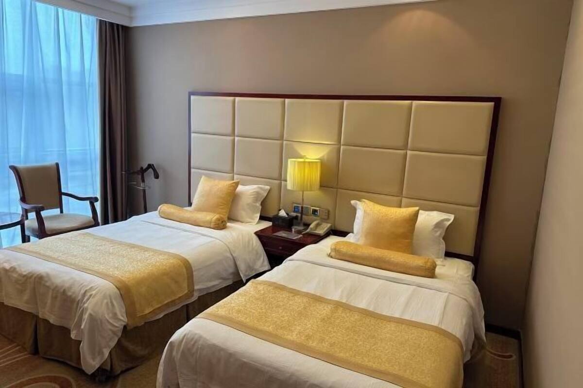A hotel room with two beds, a nightstand, a lamp, and a chair.