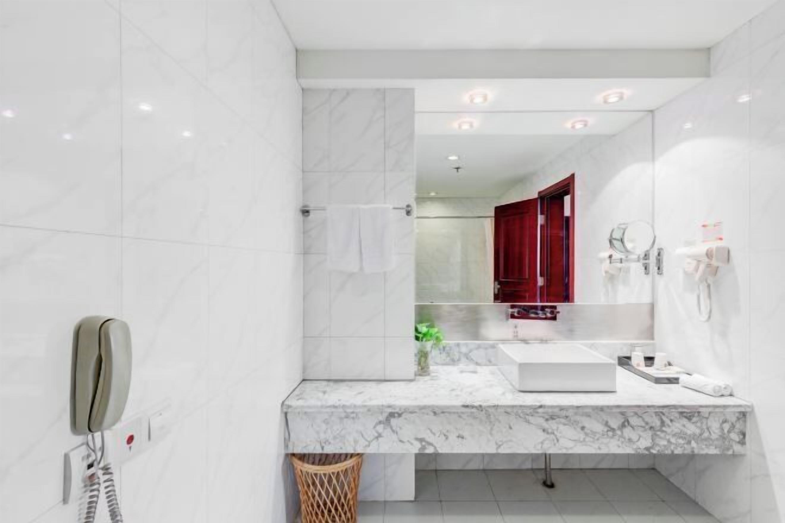 A modern bathroom with a marble sink, a mirror, a red cabinet, and a telephone.