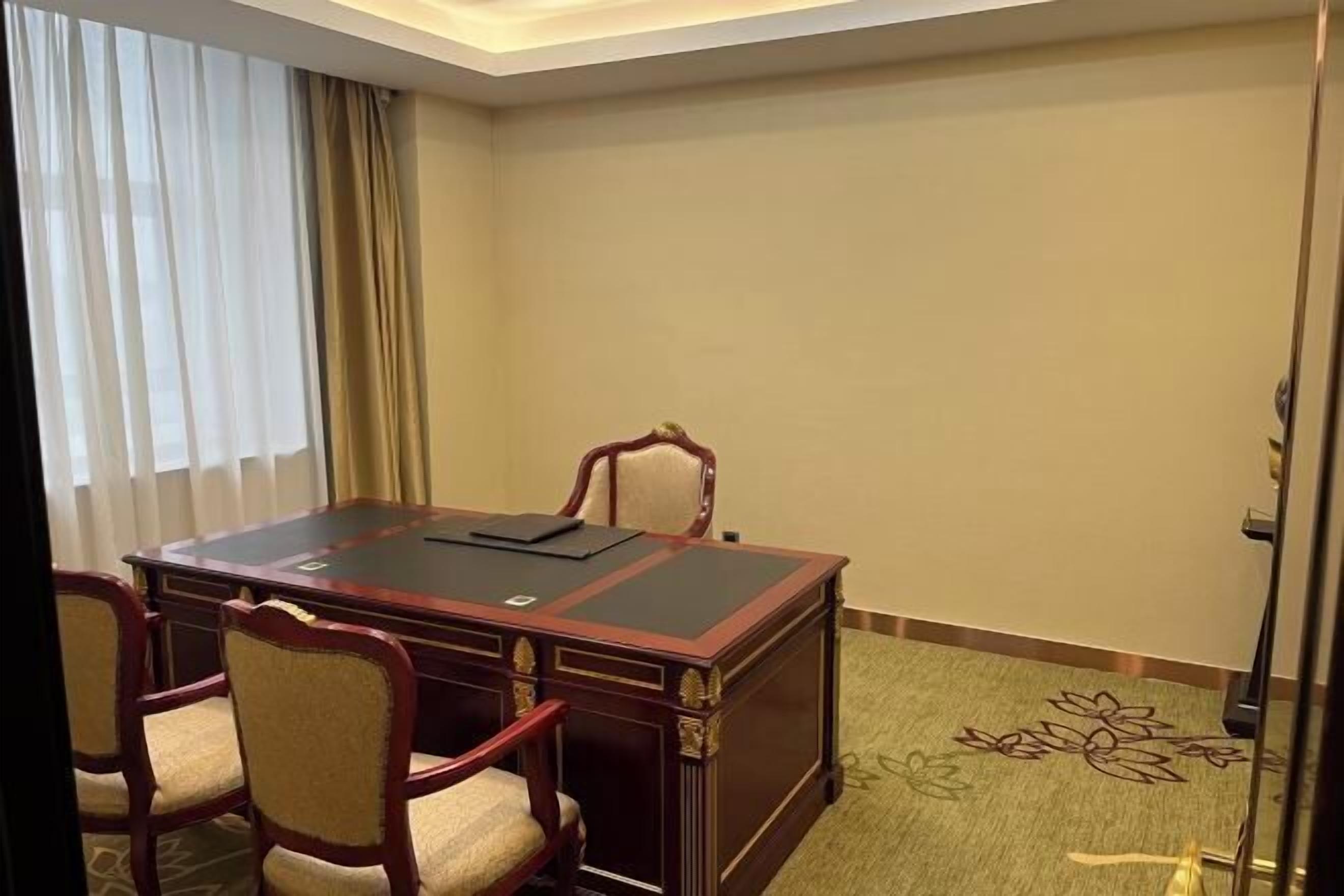 A conference room with a dark wooden table, four upholstered chairs, and a carpeted floor.