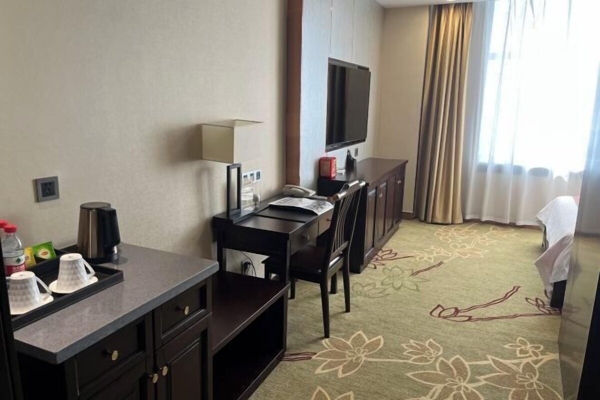 A hotel room with a desk, chair, TV, and a floral carpet.