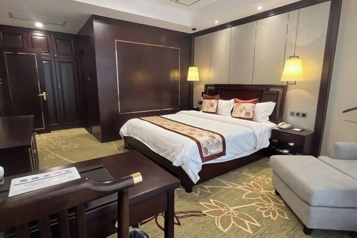 A hotel room with a bed, bedside table, lamp, and a desk with a chair.