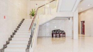 A modern hotel lobby with a marble staircase, a wooden bench, and a potted plant.
