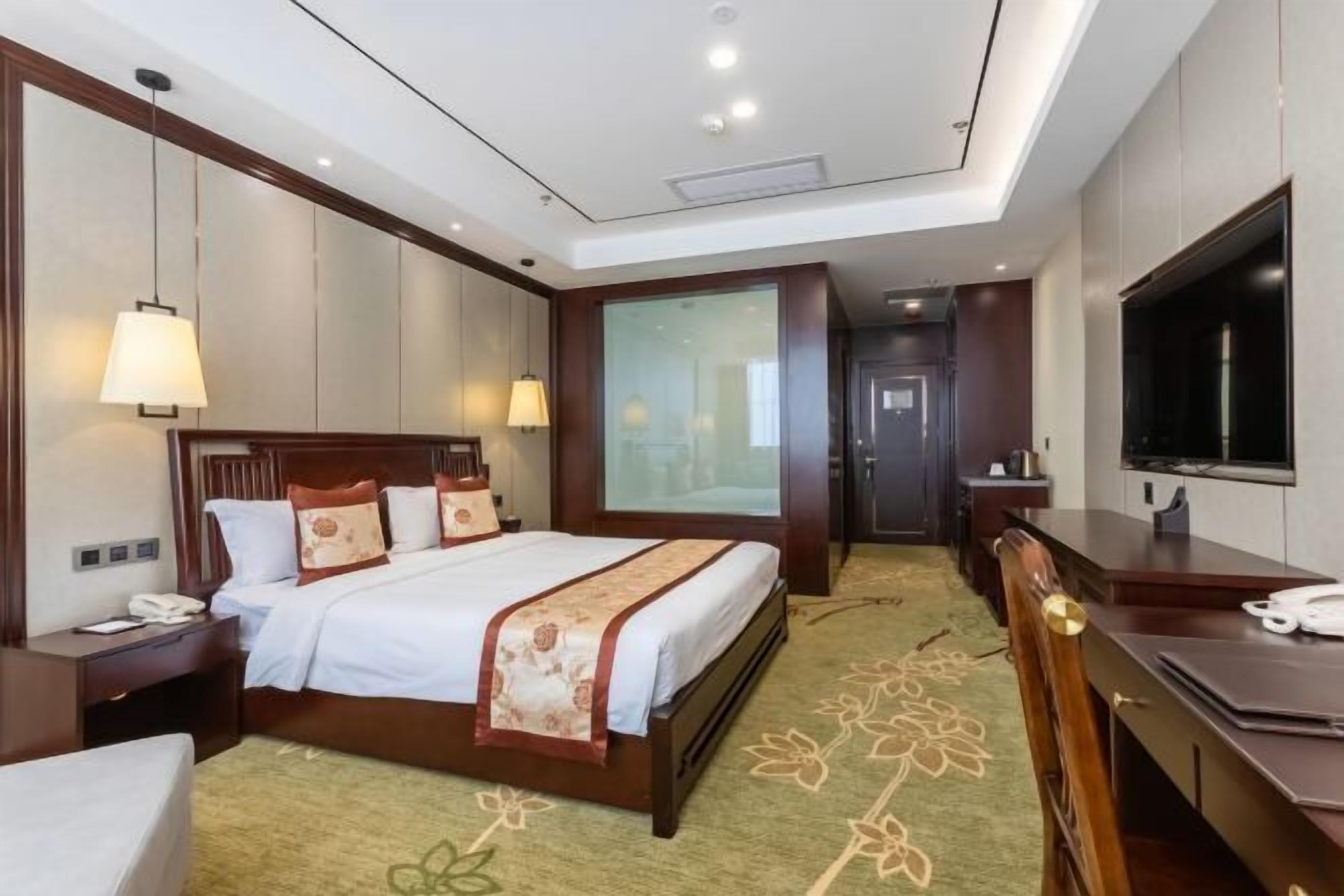 A hotel room with a large bed, bedside tables, a desk, a chair, a television, and a large window.