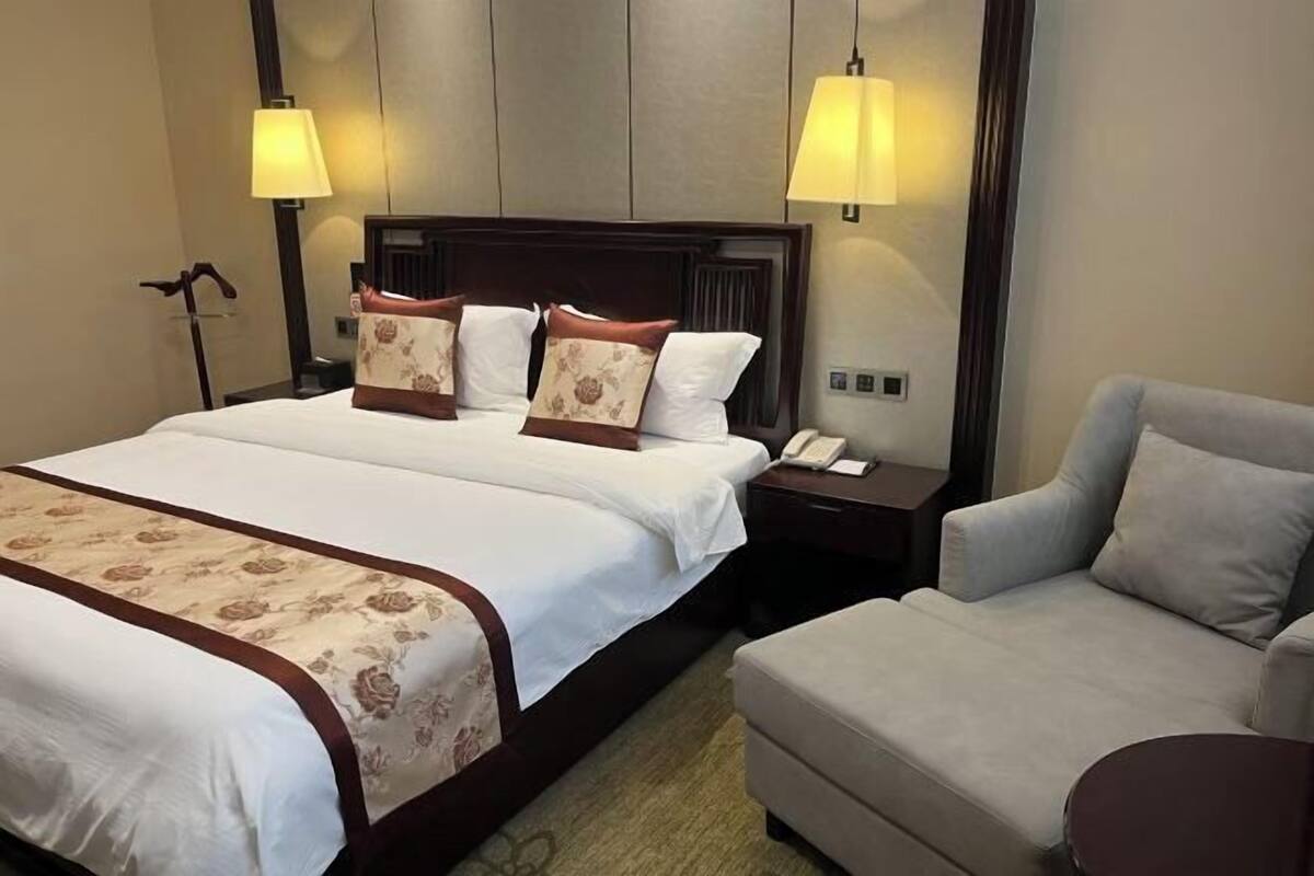 A hotel room with a large bed, two bedside lamps, a bedside phone, a sofa, and a carpeted floor.