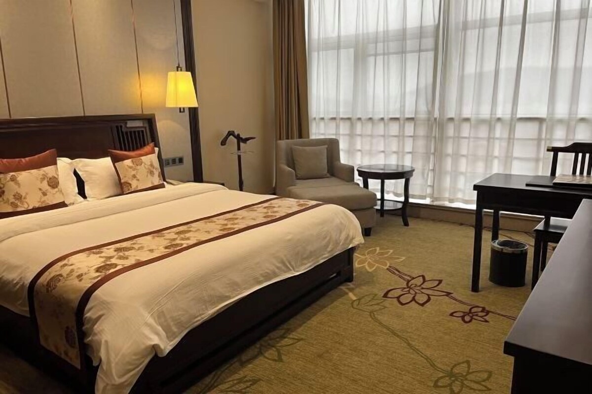 A hotel room with a large bed, a small round table, a chair, and a desk.