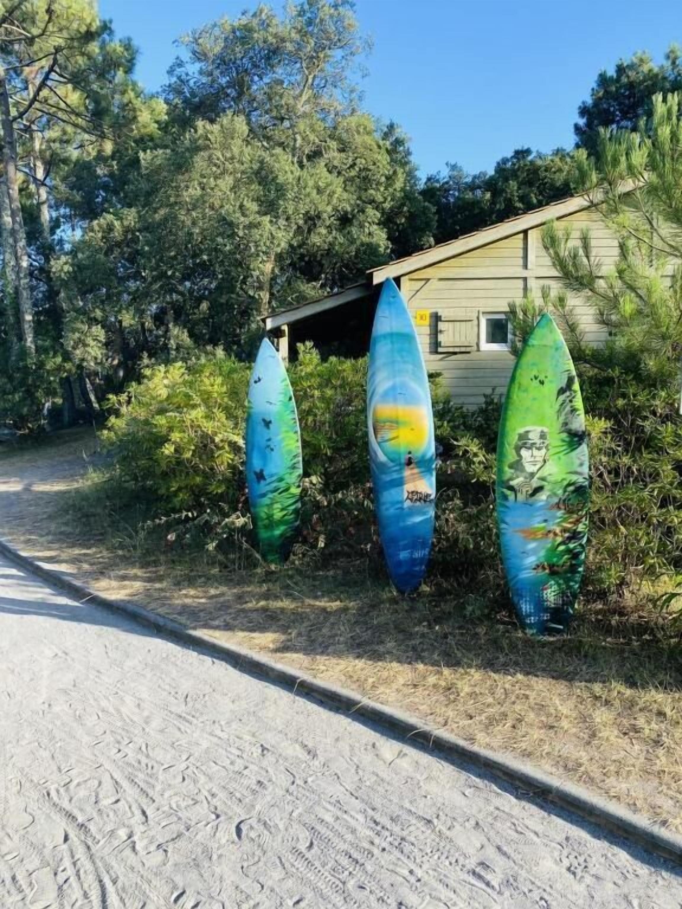 Tres tablas de surf apoyadas en un edificio, con un camino de tierra al frente.