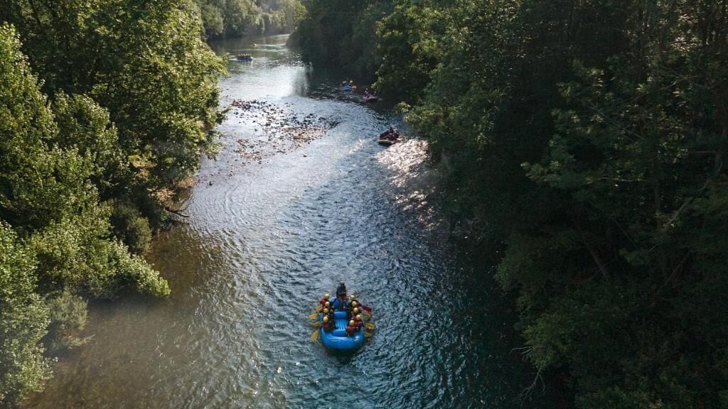Ein Fluss, umgeben von dichtem Grün, mit einem Floß, das Personen befördert.