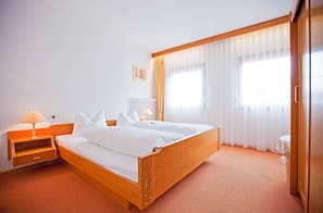 A hotel room with a wooden bed, a nightstand, a lamp, and a window with sheer curtains. - Gasthof Engel (Appenweier)