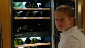 A person standing in front of a wine refrigerator with multiple shelves of wine bottles. - Gasthof Engel (Appenweier)