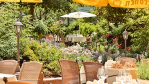 An outdoor dining area with wicker chairs and tables, surrounded by lush greenery and flowers. - Gasthof Engel (Appenweier)
