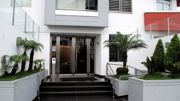 A modern building entrance with glass doors, a staircase, and potted plants. - The Comfortable Flat Miraflores (Lima)
