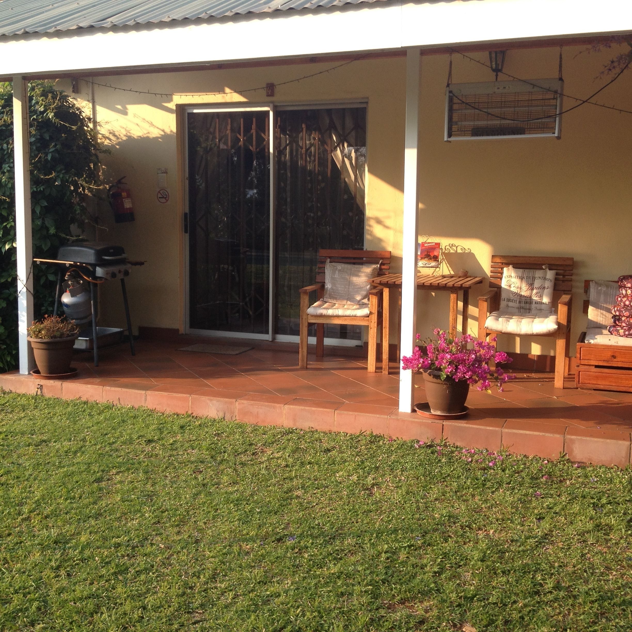 A covered patio area with a sliding glass door, two wooden chairs, a small table, and a potted plant.