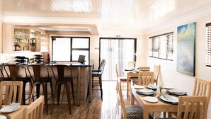Un comedor moderno con mobiliario de madera, una zona de bar con botellas y vasos, y un ventanal con persianas.