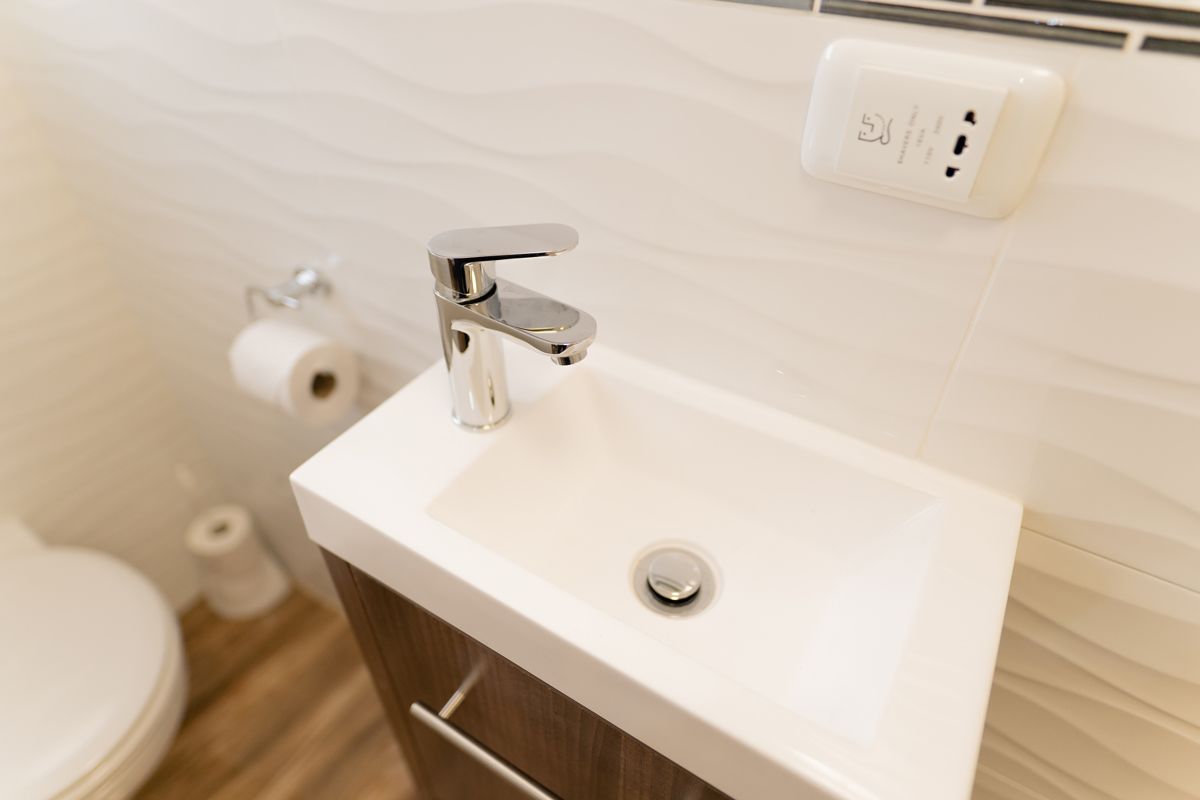 A bathroom with a white sink, a toilet, and a roll of toilet paper on the floor.